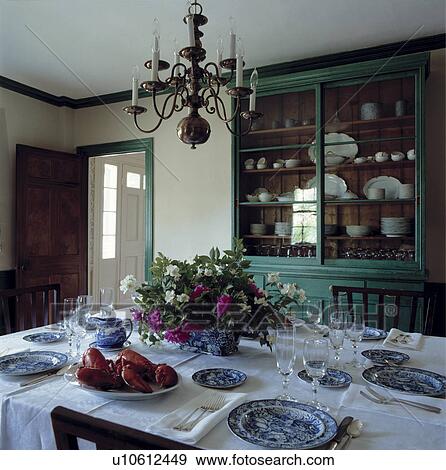 Metal chandelier above blue+white plates on white tablecloth in country diningroom with green dresser View Large Photo Image Stock Photo - Metal chandelier above blue+white plates on white tablecloth in country diningroom with green dresser. Fotosearch