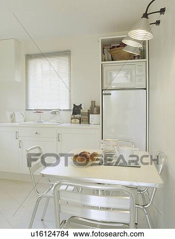 Metal lights above metal table and chairs in modern white kitchen with fitted microwave and refrigerator View Large Photo Image Picture - Metal lights above metal table and chairs in modern white kitchen with fitted microwave and refrigerator. Fotosearch