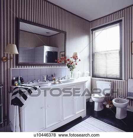 Mirror above double basins in white vanity unit in bathroom with bidet and black & white striped wallpaper View Large Photo Image Stock Photo - Mirror above double basins in white vanity unit in bathroom with bidet and black & white striped wallpaper. Fotosearch