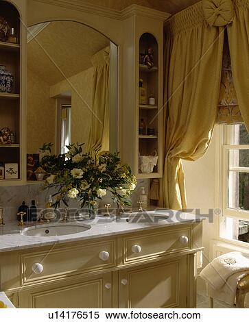 Mirror above double basins underset in marble-topped vanity unit beside window with swagged yellow curtains View Large Photo Image Stock Photography - Mirror above double basins underset in marble-topped vanity unit beside window with swagged yellow curtains. Fotosearch