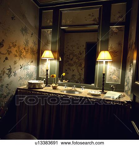 Mirror with painted floral panels above vanity unit with lighted lamps in cloakroom with hand-painted wallpaper View Large Photo Image Stock Image - Mirror with painted floral panels above vanity unit with lighted lamps in cloakroom with hand-painted wallpaper. Fotosearch
