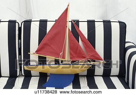 Stock Photo - Model sailing boat with red sails on black & white striped sofa. Fotosearch