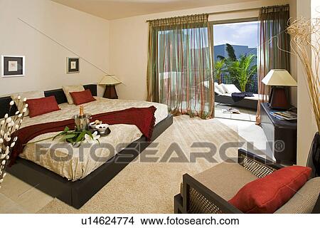 Picture - Modern bedroom with large bed and cream carpet and view of balcony through open patio doors with sheer curtains in Spanish apartment. Fotosearch