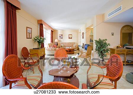 Stock Image - Modern hotel lounge with orange chairs around circular glass table with glasses and bottle of wine . Fotosearch