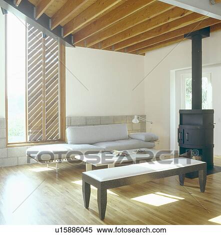 Modern stool and grey couch in architectural living room with black iron stove and smooth wood ceiling beams View Large Photo Image Stock Photography - Modern stool and grey couch in architectural living room with black iron stove and smooth wood ceiling beams. Fotosearch