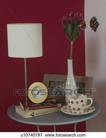 Modern white lamp and Emma Bridgewater heart-patterned cup on circular modern bedside table with clock and books View Large Photo Image Stock Photo - Modern white lamp and Emma Bridgewater heart-patterned cup on circular modern bedside table with clock and books. Fotosearch