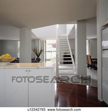 Modern white openplan hall kitchen with white open-tread staircase and polished wooden flooring View Large Photo Image Stock Image - Modern white openplan hall kitchen with white open-tread staircase and polished wooden flooring. Fotosearch