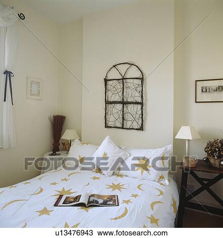 Stock Image - Moon & star motif on white pillowsand duvet in modern white bedroom with twig sculpture above bed. Fotosearch