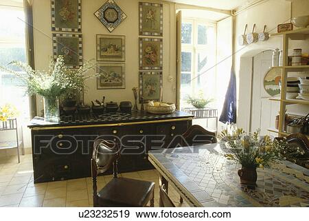 Stock Photo - Mosaic-topped table and large black sideboard below group of pictures in French dining room. Fotosearch