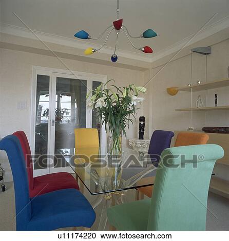 Multi-coloured modern lighting above glass table with brightly coloured upholstered chairs in white dining room View Large Photo Image Stock Image - Multi-coloured modern lighting above glass table with brightly coloured upholstered chairs in white dining room. Fotosearch