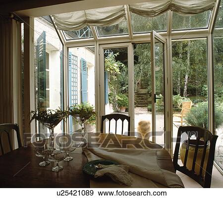 Stock Photo - Napkins and glasses on table in conservatory dining room with view of garden through patio doors. Fotosearch