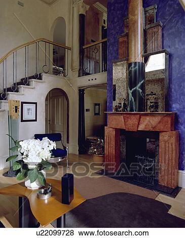 Stock Photo - Neoclassical marbled red fireplace on blue wall in large hall with modern table and patterned wooden flooring. Fotosearch