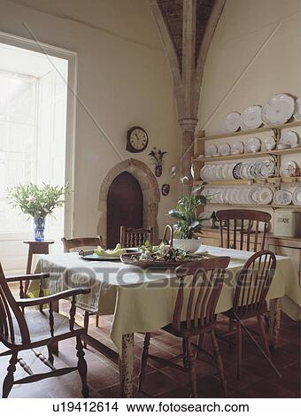 Old pine chairs around square table with cream cloth in country dining room with platerack on the wall View Large Photo Image Picture - Old pine chairs around square table with cream cloth in country dining room with platerack on the wall. Fotosearch