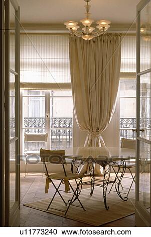 Open doors to circular metal and wood table in diningroom with cream curtain between French windows View Large Photo Image Stock Image - Open doors to circular metal and wood table in diningroom with cream curtain between French windows. Fotosearch