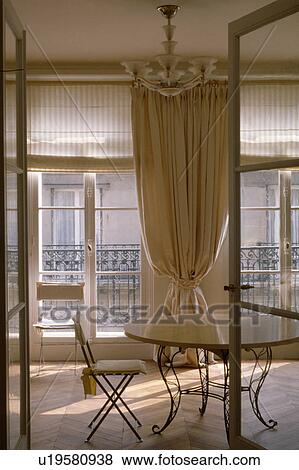 Open doors to circular metal and wood table in diningroom with cream curtain between French windows View Large Photo Image Stock Photo - Open doors to circular metal and wood table in diningroom with cream curtain between French windows. Fotosearch