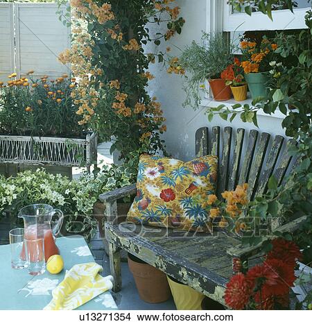 Orange bougainvillea on pillar beside rustic wooden bench with colourful cushion on patio in front of window View Large Photo Image Picture - Orange bougainvillea on pillar beside rustic wooden bench with colourful cushion on patio in front of window. Fotosearch