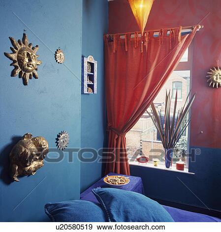 Orange curtain at window in turquoise and pink bedroom with gilt celestial motifs on wall above bed View Large Photo Image Stock Photo - Orange curtain at window in turquoise and pink bedroom with gilt celestial motifs on wall above bed. Fotosearch