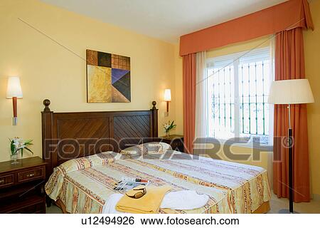 Orange curtains at window in pale yellow bedroom with yellow patterned linen on mahogany bed View Large Photo Image Stock Photograph - Orange curtains at window in pale yellow bedroom with yellow patterned linen on mahogany bed. Fotosearch