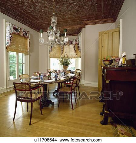 Ornate ceiling and glass chandelier above table with place settings in dining room with wood flooring and cane blinds View Large Photo Image Picture - Ornate ceiling and glass chandelier above table with place settings in dining room with wood flooring and cane blinds. Fotosearch