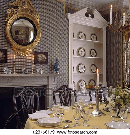 Ornate circular gilt mirror above fireplace in dining room with grey striped wallpaper and white dresser in alcove View Large Photo Image Stock Photo - Ornate circular gilt mirror above fireplace in dining room with grey striped wallpaper and white dresser in alcove. Fotosearch