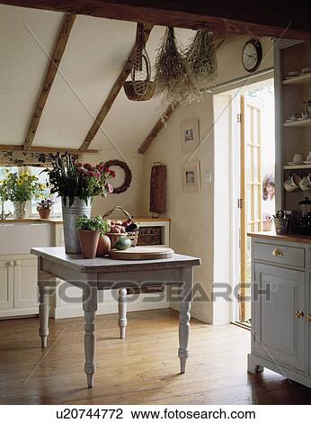 Stock Image - Painted grey wooden table in cottage kitchen with sloping ceiling and wooden flooring. Fotosearch