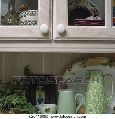 Stock Photography - Pale green jugs on worktop below glazed kitchen cupboard doors. Fotosearch