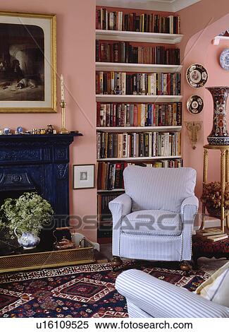 Pale striped armchair in front of bookshelves in pink living room with patterned rug in front of cast iron fireplace View Large Photo Image Stock Photography - Pale striped armchair in front of bookshelves in pink living room with patterned rug in front of cast iron fireplace . Fotosearch