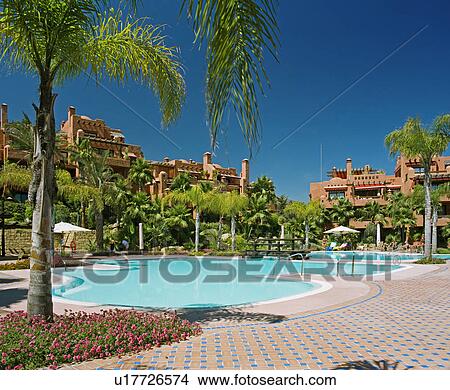 Palm trees and blue and terracotta tiles around turquoise swimmingpool with terracotta Spanish holiday village in background View Large Photo Image Picture - Palm trees and blue and terracotta tiles around turquoise swimmingpool with terracotta Spanish holiday village in background. Fotosearch