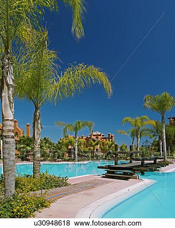 Palm trees and wooden bridge over turquoise swimmingpools in Spanish holiday village View Large Photo Image Stock Photo - Palm trees and wooden bridge over turquoise swimmingpools in Spanish holiday village. Fotosearch