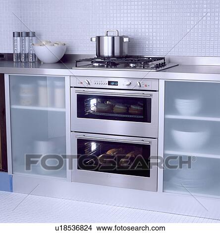 Pan on hob above stainless steel double oven in kitchen unit with opaque glass doors View Large Photo Image Picture - Pan on hob above stainless steel double oven in kitchen unit with opaque glass doors . Fotosearch