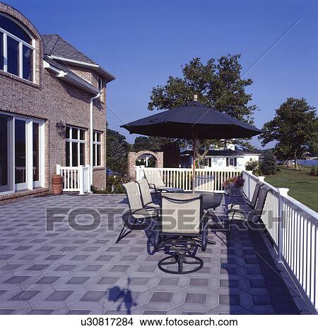 Picture - Parasol above table and chairs on paved terrace of modern country house. Fotosearch