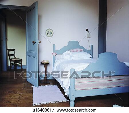 Stock Photo - Pastel blue painted wooden bed in simple white country bedroom with wooden floor and pastel blue door. Fotosearch