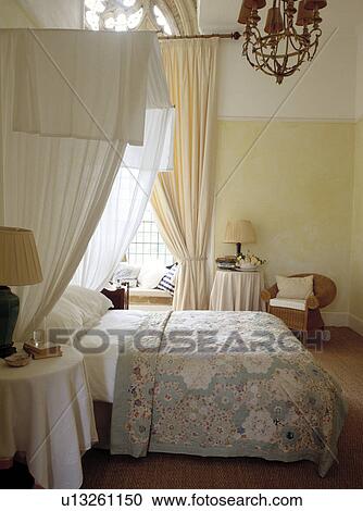 Pastel patchwork quilt on half-tester bed with white drapes in country bedroom with cream curtains View Large Photo Image Stock Image - Pastel patchwork quilt on half-tester bed with white drapes in country bedroom with cream curtains. Fotosearch