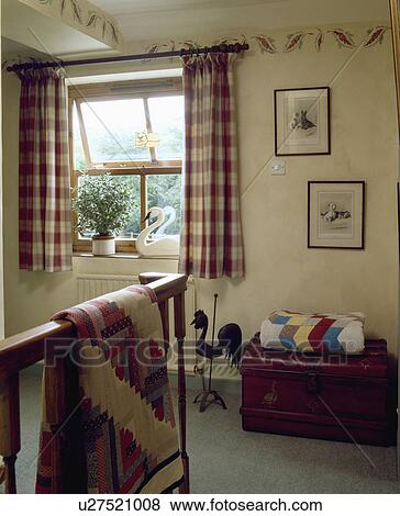 Stock Photo - Patchwork quilts on bannisters and wooden chest on small landing with checked curtains at the window. Fotosearch