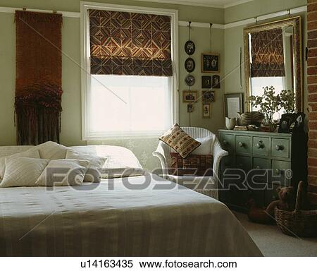Stock Photography - Patterned blind on window in bedroom with white Lloyd Loom chair and white cushions and bedcover. Fotosearch