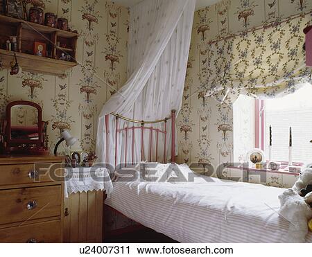 Patterned Wallpaper And Blind In Teenager Girls Bedroom With White Drapes On Pink Single Brass Bed Stock Image