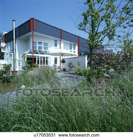 Stock Image - Paved path through long grass to modern white house in the country. Fotosearch