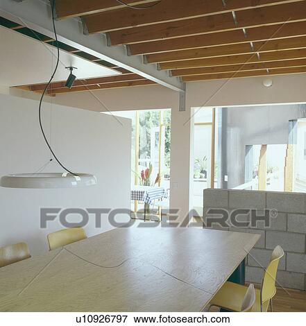 Pendant light above pale wood table in modern openplan city dining room with smooth ceiling beams View Large Photo Image Stock Photo - Pendant light above pale wood table in modern openplan city dining room with smooth ceiling beams. Fotosearch
