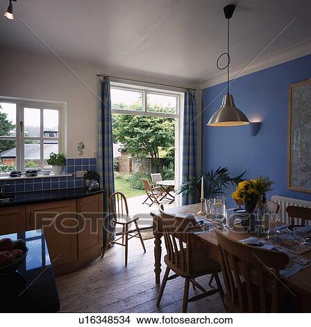 Pendant light above pine table and chairs in blue kitchen with wooden flooring and doors open to garden View Large Photo Image Picture - Pendant light above pine table and chairs in blue kitchen with wooden flooring and doors open to garden. Fotosearch
