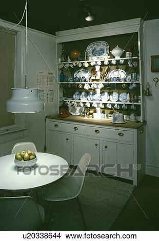 Pendant light over white circular table and polypropylene chairs in seventies dining room with traditional white dresser View Large Photo Image Picture - Pendant light over white circular table and polypropylene chairs in seventies dining room with traditional white dresser. Fotosearch