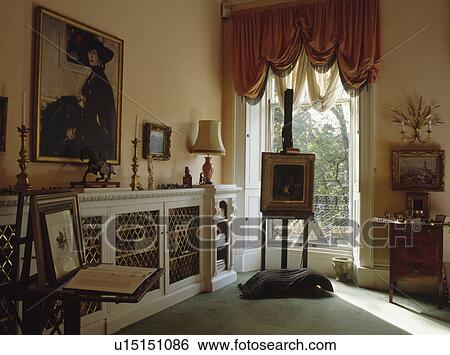 Picture on easel in front of tall window in townhouse living room with large oil painting above bookshelves View Large Photo Image Stock Photograph - Picture on easel in front of tall window in townhouse living room with large oil painting above bookshelves. Fotosearch