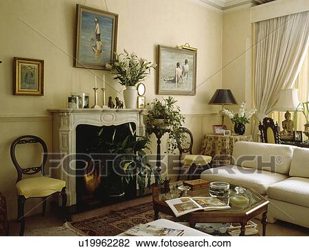 Stock Image - Pictures above fireplace in cream living room with white sofa. Fotosearch