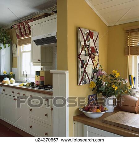 Stock Photo - Pinboard above worktop in yellow kitchen extension. Fotosearch