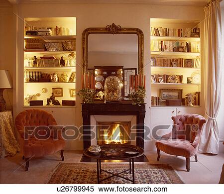 Pink armchairs on either side of fireplace in traditional living room with lighted alcove shelves View Large Photo Image Stock Photography - Pink armchairs on either side of fireplace in traditional living room with lighted alcove shelves. Fotosearch
