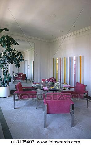 Stock Image - Pink suede and steel chairs and circular glass table in modern sixties dining room with grey carpet. Fotosearch