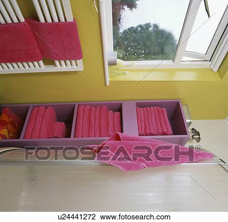 Stock Image - Pink towels stacked on purple shelf unit in yellow bathroom with white radiator. Fotosearch