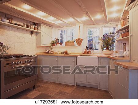 Stock Image - Range oven and white ceramic sink in white cottage kitchen with pale grey fitted cupboards. Fotosearch
