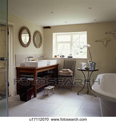 Stock Image - Rectangular white basins on wooden unit with storage baskets in modern white bathroom with white tiled floor. Fotosearch