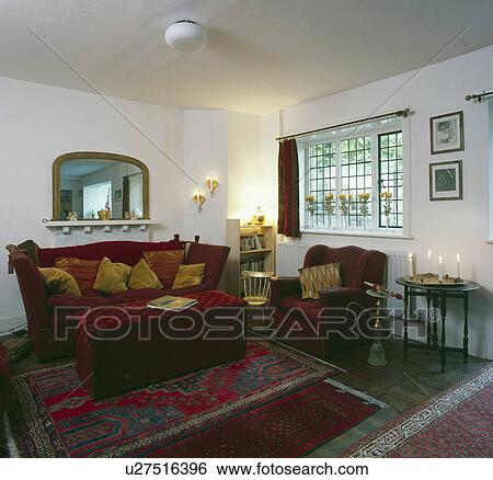 Stock Photograph - Red and gold cushions on red sofa below mirror in living room. Fotosearch