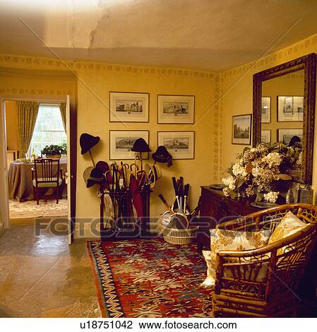 Stock Image - red oriental carpet in yellow hall with collection of walking sticks and umbrellas in stand beside open door with view of diningroom. Fotosearch